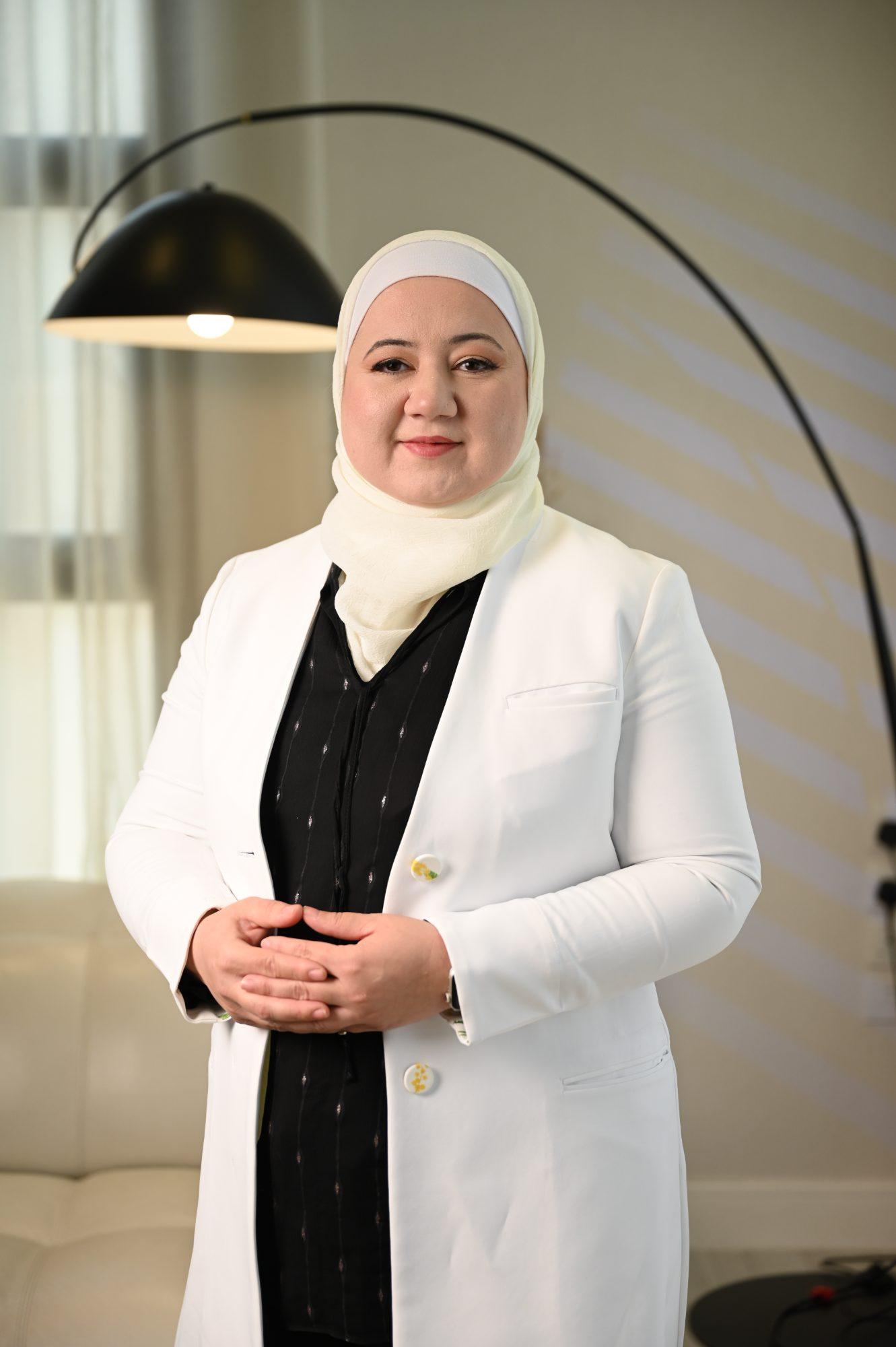 د. دانا أبوروائح واقفة بالمعطف الأبيض، ويداها متشابكتان أمامها